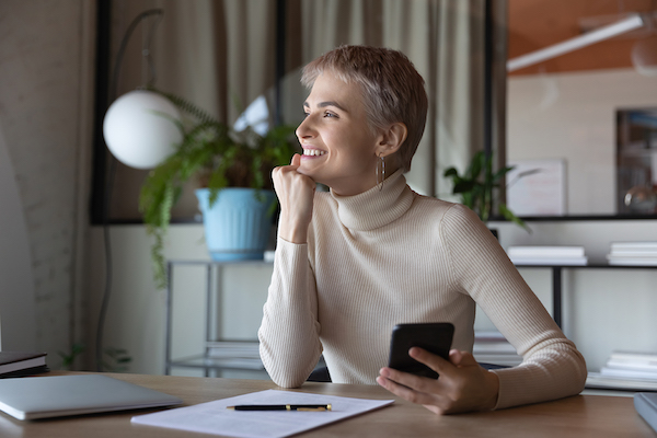 A middle aged woman holding her phone smiles while sitting at a table